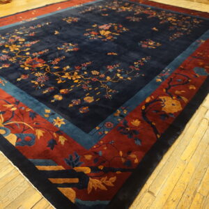 Navy floral rug with thick red and teal borders displayed on rustic yellow wood flooring.