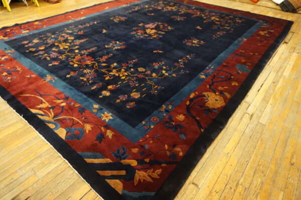 Navy floral rug with thick red and teal borders displayed on rustic yellow wood flooring.
