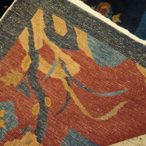 Flat-weave rug with rust and navy geometric patterns is folded over a dark blue plush rug.