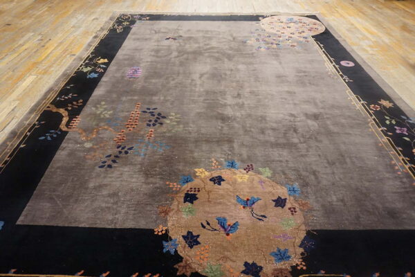 Gray high-pile rug with a detailed multicolored floral design and black border on a wood floor.
