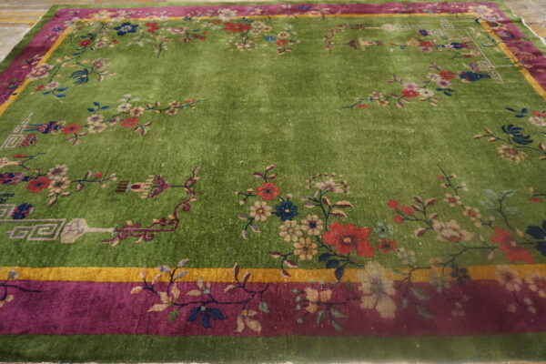 Green high-pile rug with colorful floral vines, magenta borders, and a solid center on wood flooring.