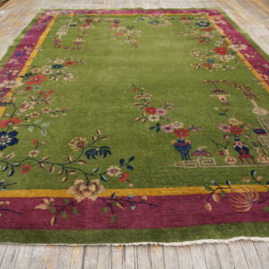 Vibrant green floral rug with magenta and yellow borders covers distressed light wood flooring.