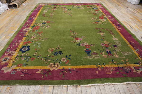 Vibrant green floral rug with magenta and yellow borders covers distressed light wood flooring.