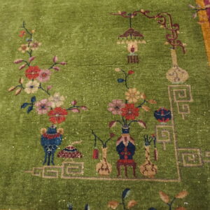 Detailed view of a moss green rug with stylized floral motifs, decorative objects, and a maroon and gold border.