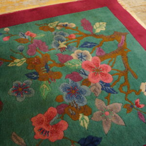 Carved green rug with magenta border shows pink, blue, and brown florals on wood planks.