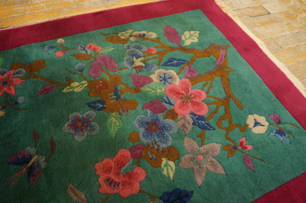 Carved green rug with magenta border shows pink, blue, and brown florals on wood planks.