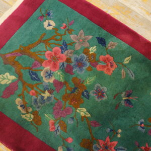 Teal rug featuring a vibrant flowering branch pattern, magenta border, and light distressed wood flooring.