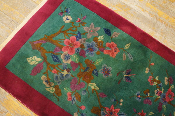 Teal rug featuring a vibrant flowering branch pattern, magenta border, and light distressed wood flooring.