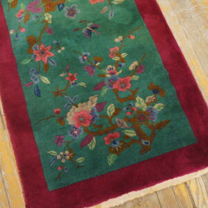 Teal, high-pile rug with multicolor floral branches and a wide maroon border rests on distressed wooden floorboards.