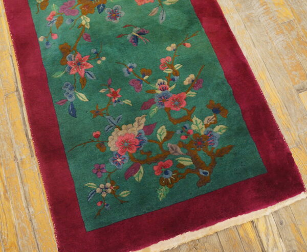 Teal, high-pile rug with multicolor floral branches and a wide maroon border rests on distressed wooden floorboards.