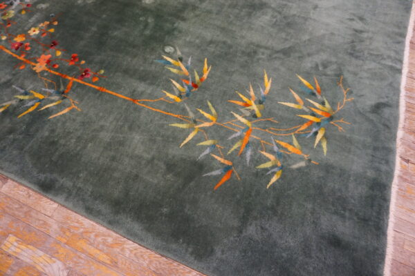 Deep green high-pile rug with colorful floral and bamboo patterns rests on worn wooden planks.