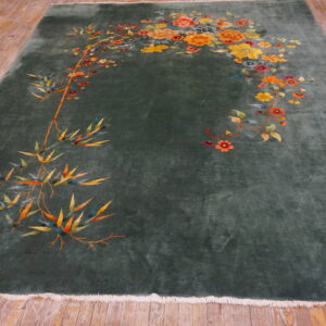 Dark green rug featuring vibrant orange and yellow bamboo and floral motifs displayed on light wood flooring.