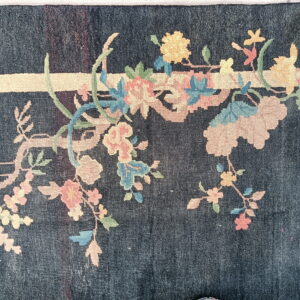 Low-pile dark blue rug features sprawling branches of pastel pink, yellow, and blue flowers.