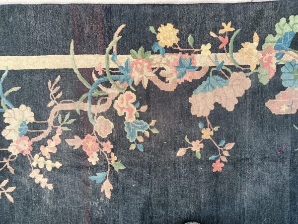 Low-pile dark blue rug features sprawling branches of pastel pink, yellow, and blue flowers.