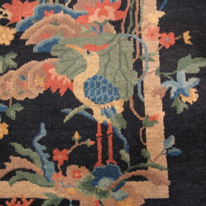 Black rug detail showing a multicolored stylized crane and floral pattern bordered in beige on a wood floor.