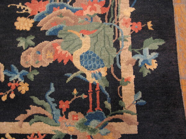 Black rug detail showing a multicolored stylized crane and floral pattern bordered in beige on a wood floor.