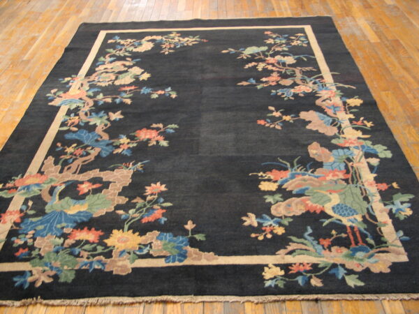 Dark rug with a multicolored floral and bird border and light frame on worn wood flooring.