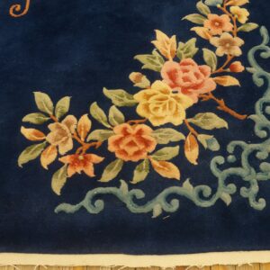 Dark blue rug with pink and yellow floral motif and light blue scrolling border on wood flooring.