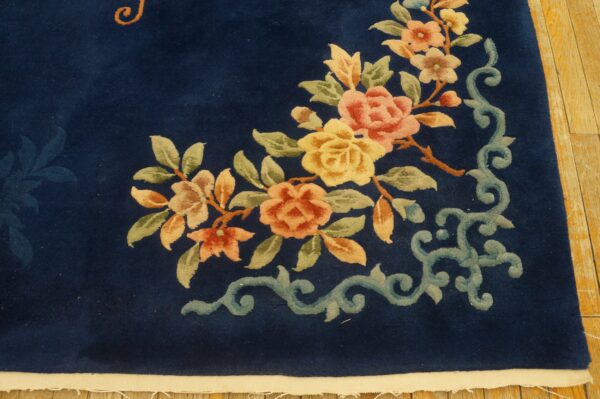 Dark blue rug with pink and yellow floral motif and light blue scrolling border on wood flooring.