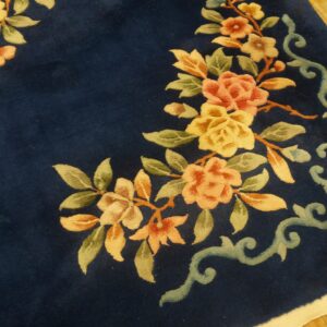 Close-up of a carved navy blue rug featuring yellow and peach floral motifs on wood flooring.