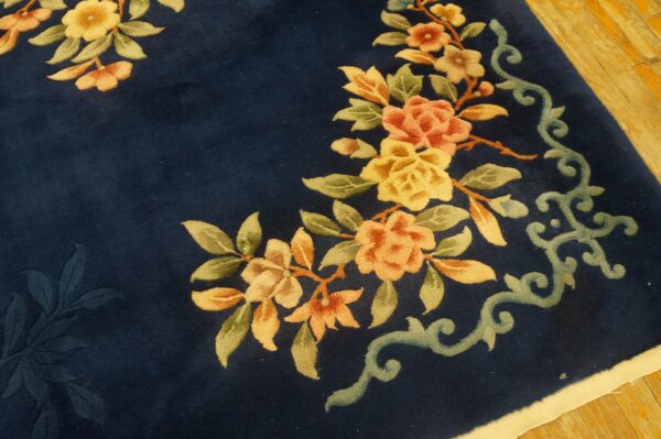Close-up of a carved navy blue rug featuring yellow and peach floral motifs on wood flooring.