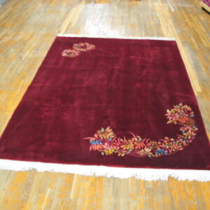 Burgundy rug with a high-sheen pile and white fringe displays colorful floral sprays on a wood floor.