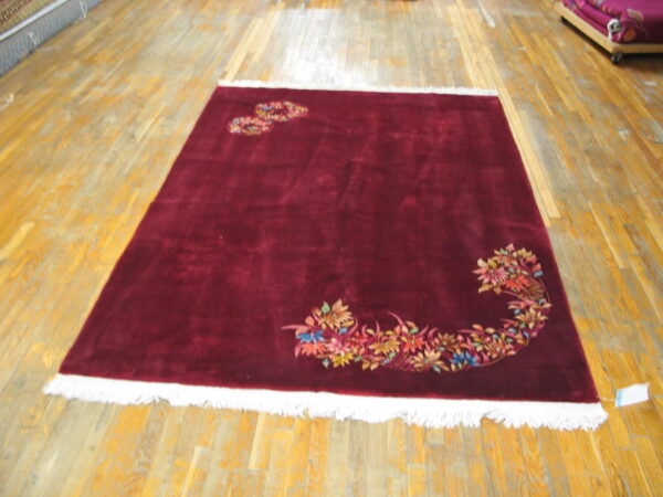 Burgundy rug with a high-sheen pile and white fringe displays colorful floral sprays on a wood floor.