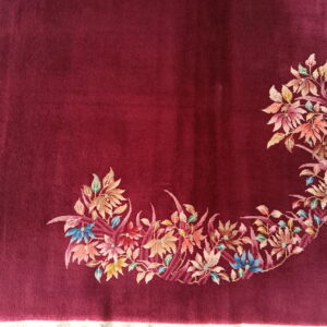 Plush maroon rug featuring a dense, curving border of floral motifs in pink, gold, and blue.