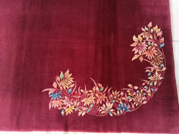 Plush maroon rug featuring a dense, curving border of floral motifs in pink, gold, and blue.