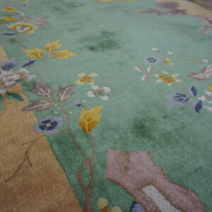 Close-up of a floral rug with a pale mint green field and a golden tan border.