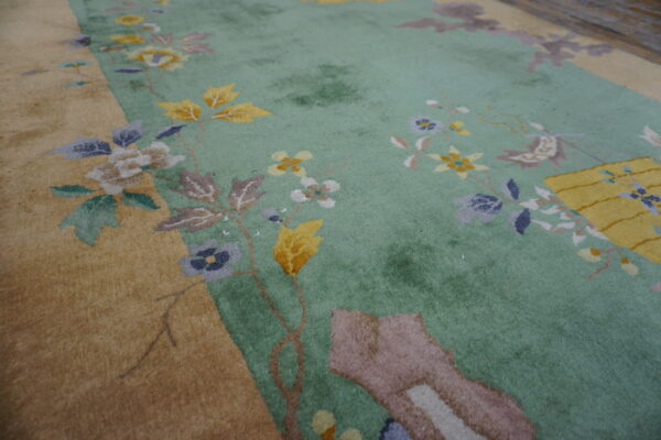 Close-up of a floral rug with a pale mint green field and a golden tan border.