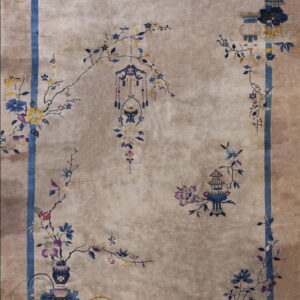 Taupe rug with a low pile, featuring a blue border and detailed floral vines, vases, and hanging lanterns.