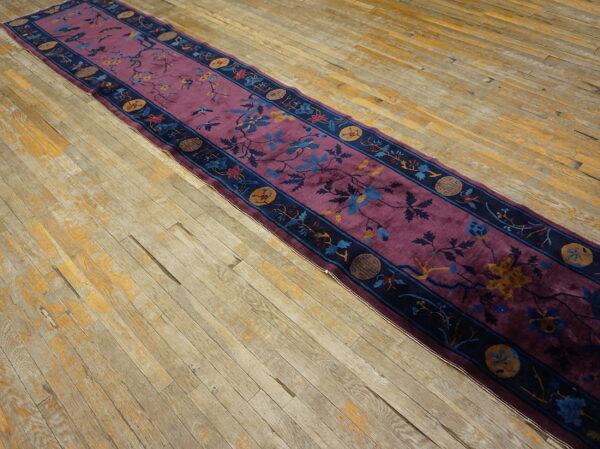 Deep purple runner rug featuring a navy border and blue floral designs rests on worn wooden flooring.