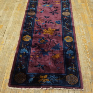 Plum runner rug featuring a botanical pattern and dark navy border on distressed wood flooring.