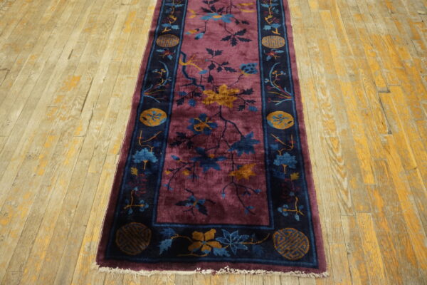 Plum runner rug featuring a botanical pattern and dark navy border on distressed wood flooring.