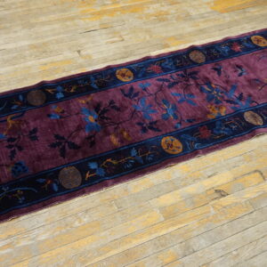 A low-pile purple rug runner with blue and gold floral patterns rests on distressed blonde wood flooring.