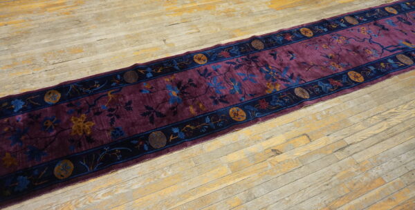 A low-pile purple rug runner with blue and gold floral patterns rests on distressed blonde wood flooring.