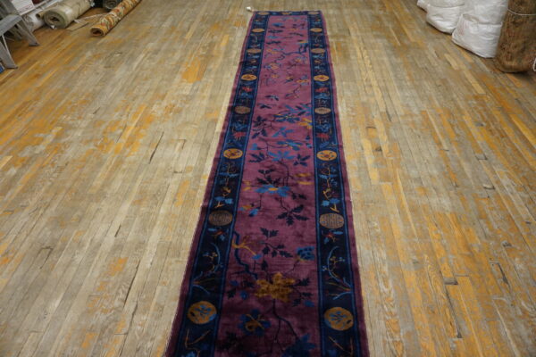 An oriental purple runner with blossoming branches and a navy medallion border is displayed on worn wood planks.