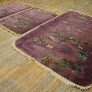 A set of three velvety purple rugs with colorful floral borders rests on rustic wood flooring.