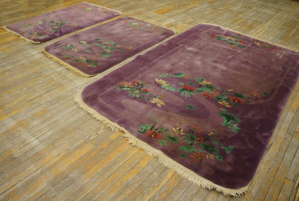 A set of three velvety purple rugs with colorful floral borders rests on rustic wood flooring.