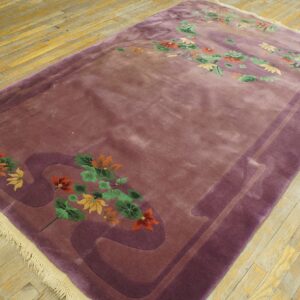 Plush mauve rug featuring carved purple borders and multicolored floral motifs on yellow-toned wood flooring.
