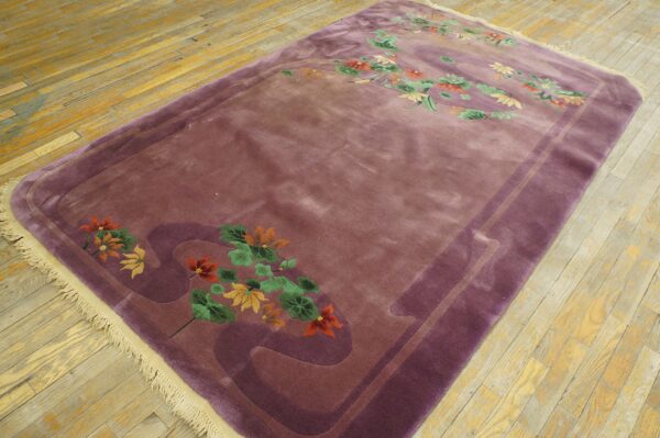 Plush mauve rug featuring carved purple borders and multicolored floral motifs on yellow-toned wood flooring.