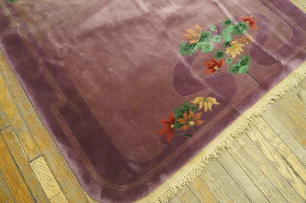 Plush mauve rug with orange and green floral motifs and sculpted borders on light hardwood flooring.