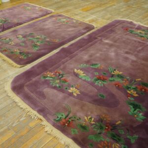 Three high-pile mauve rugs with colorful floral carvings are displayed on distressed plank wood flooring.