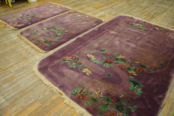 Three high-pile mauve rugs with colorful floral carvings are displayed on distressed plank wood flooring.