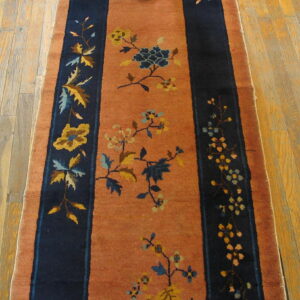 Terracotta runner rug featuring navy blue stripes and yellow and blue floral vine patterns on wood planks.