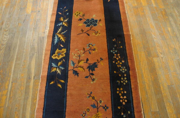 Terracotta runner rug featuring navy blue stripes and yellow and blue floral vine patterns on wood planks.