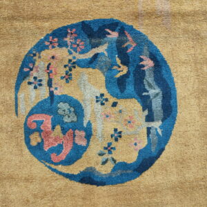 Textured camel rug with a circular medallion displaying blue, coral, and gray stylized figures and florals.