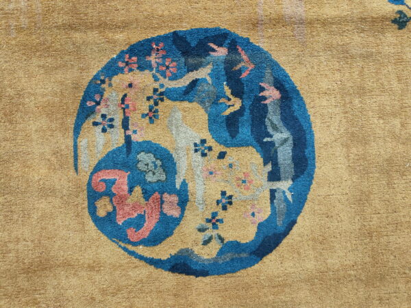 Textured camel rug with a circular medallion displaying blue, coral, and gray stylized figures and florals.