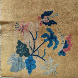 Golden rug displaying a multicolored floral and butterfly design over white square tiles.